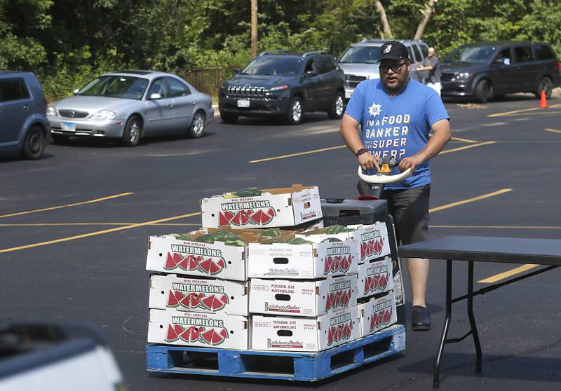 As people wait to pict up food boxes as  Calvin Yurko unloads food from a Northern Illinois Food Pantry truck before the start of a mobile food pantry stop at St. Ann's Episcopal Church, 503 West Jackson St, in Woodstock, Monday, July 11, 2022. On average the this mobile food pantry delivers enough to feed around 225 families every other week.