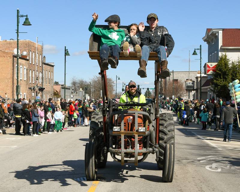 Kyle Lipowski with the Hillbilly Social Club of Lockport drives a 1956 International Harvester 300 Utility while Jackson Mukenschnabl, 11, of Lockport, Kaila Lipowski, 6, Lockport and David Mcmanus, 13, of Wilmington wave as they ride in the bucket during the Lemont St. Patrick’s parade on Saturday March 9, 2024.