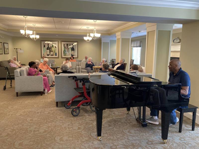 The residents of The Reserve of Geneva - Independent Living Community listen to a piano player and relax together.