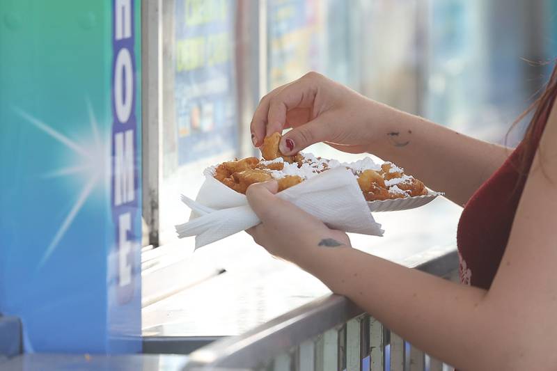 An event goer digs into their funnel cake while waiting to pay at the Taste of Joliet on Saturday, June 22, 2024 at Joliet Memorial Stadium.