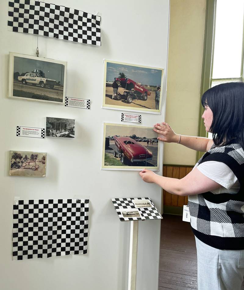 Little White School Museum assistant Emily Dutton makes a last-minute adjustment on one of the display panels for “SUNDAY! SUNDAY! SUNDAY!”, a new temporary exhibit available through September, featuring the Oswego Drag Raceway at the museum, 72 Polk St.