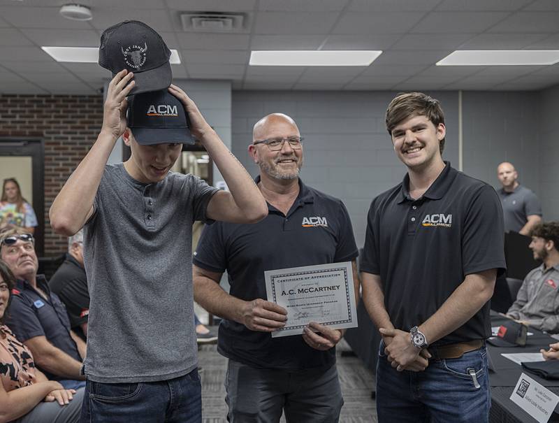 Issac Fleming of Fulton High School  slips on the hat of his new employer AC McCartney Friday, May 17, 2024. Scott Noller (left) and Luke McCartney represent the business.