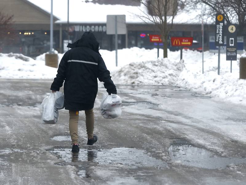 A woman carries groceries as she navigates an icy parking lot in Spring Grove on Tuesday, Jan. 23, 2023. Residents throughout northern Illinois woke up to icy and slippery roads.