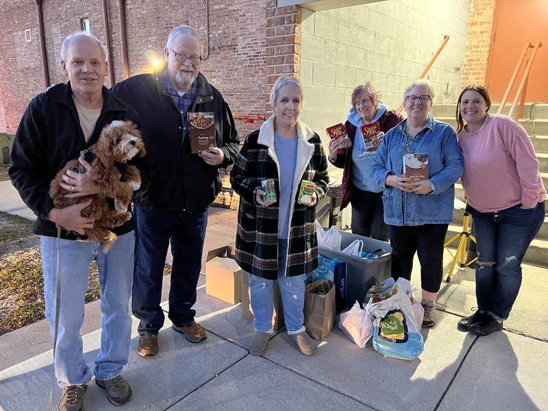 Dave Pearson (holding Beau Pearson), Bernie Schumeman, Patti Pearson, Gloria Dennison, Nancy Schumeman and Angela Schiola–Niemeyer stand outside Stage Coach Players in DeKalb on Tuesday, November 14 for the last day of the troupe's Thanksgiving food drive.