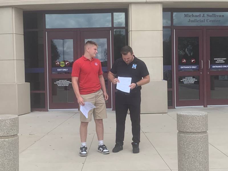 Marian Central Catholic High School wrestler Jimmy Mastny, left, and coach Jordan Blanton stand outside the McHenry County courthouse on Sept. 6, 2024, with copies of the ruling that overturned their IHSA suspensions.