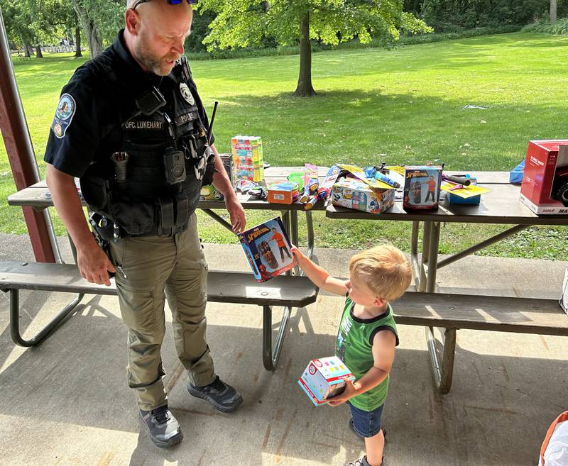 Caleb Watson, 18 months, of Prophetstown, hands a Spiderman punching bag back to Prophetstown Police Officer Will Lakehart, opting for sidewalk chalk instead at the 18th annual Dick Brown Fishing Derby, held at Prophetstown State Park on Saturday, June 15, 2024.
