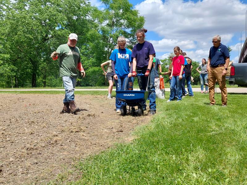 David Raikes advises Milton Pope eighth graders Lylah Hebel and Emma Peterson on how to spread seed into a plot Wednesday, May 22, 2024, at Illini State Park in Marseilles.