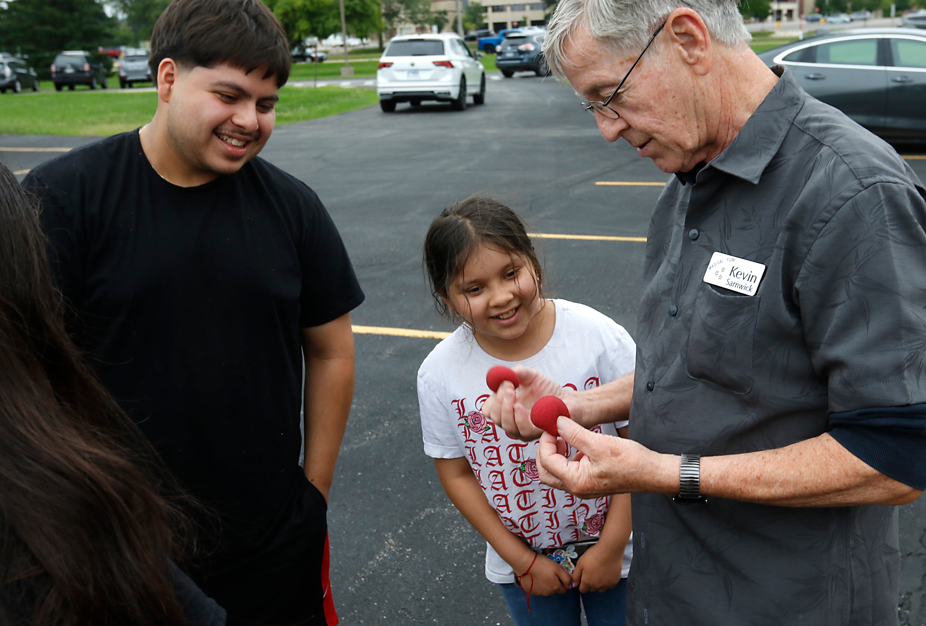 Eder Estada and Jamileth Estrada watch as Kevin Sarnwick performs a magic trick during a Woodstock School District 200 Back to School Coming to You event at Northwood Middle School on Tuesday, Aug. 6, 2024. The location was one of twelve stops on the tour that gave out backpacks and school supplies, provided registration help and computer repair.