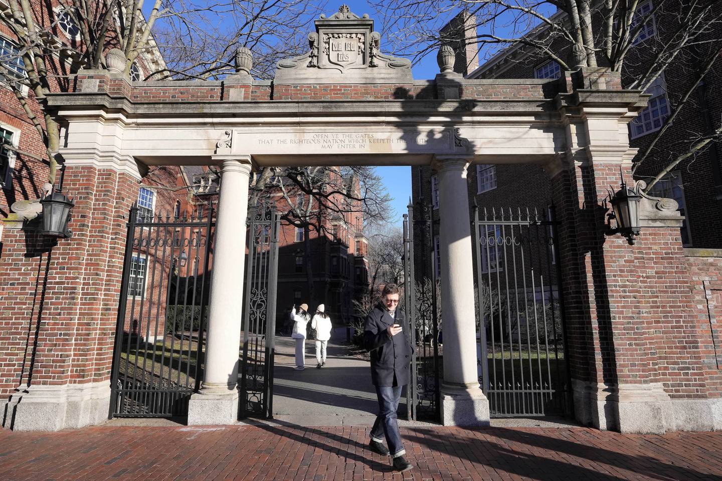 FILE - A passer-by walks through a gate to the Harvard University campus, Jan. 2, 2024, in Cambridge, Mass. As more than 2 million graduating high school students from across the United States finalize their decisions on what college to attend this fall, many are facing jaw-dropping costs — in some cases, as much as $95,000.