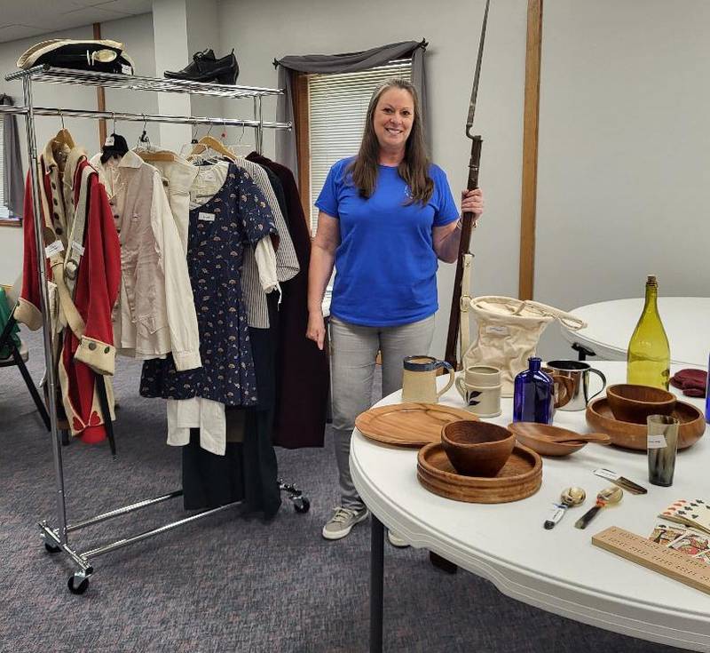 Barbara Peterson, program presenter at the September Chief Senachwine DAR Chapter meeting, displays clothes and period items from reenacting Revolutionary War battles. She holds a "Brown Bess" musket and displays a British uniform since reenactors portray both sides of battles.