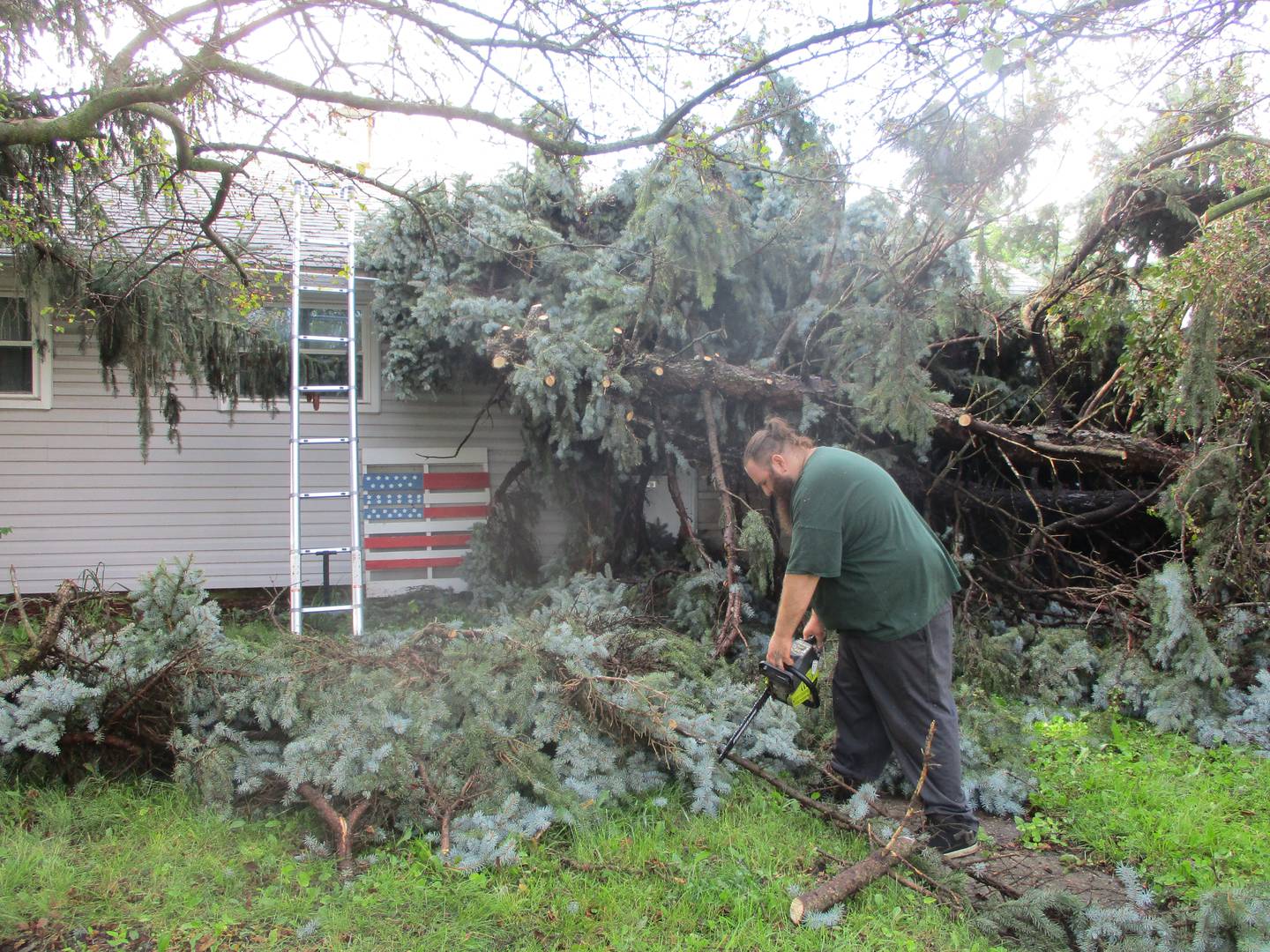 Nathaniel Crider used a power saw Tuesday to cut up a tree that fell from a neighbors yard onto his Webster Avenue house in the Marycrest neighborhood of Joliet during the storm the night before. July 16, 2024