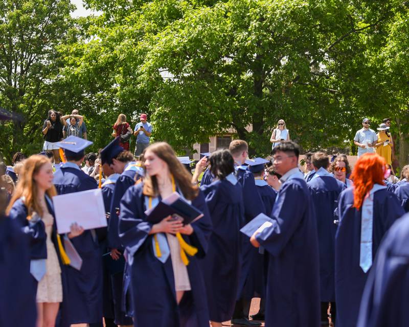 Friends and family members stand on a hill looking for their graduates after the Downers Grove South graduation on Sunday May 19, 2024, held at Downers Grove South High School.