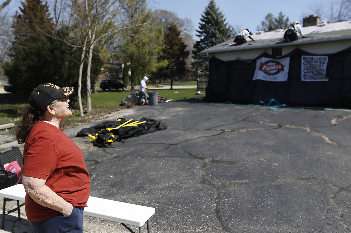 U.S. Army veteran Robin Waltrip watches as workers Feldco replace the roof on her home in Island Lake on Monday April 8, 2024, as part of the Owens Corning Roof Deployment Project. The Owens Corning Foundation is donating roofing materials and Feldco is donating the labor.