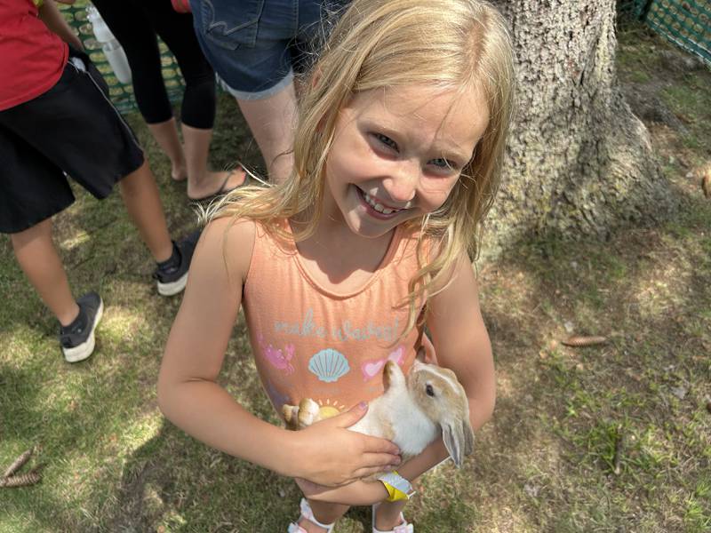 Millie Eddy, 7, of Channahon, is all smiles as she holds a bunny rabbit at Kriss' Funny Farm & Wedding Barn's petting zoo during German Valley Days on Saturday, July 20,, 2024.