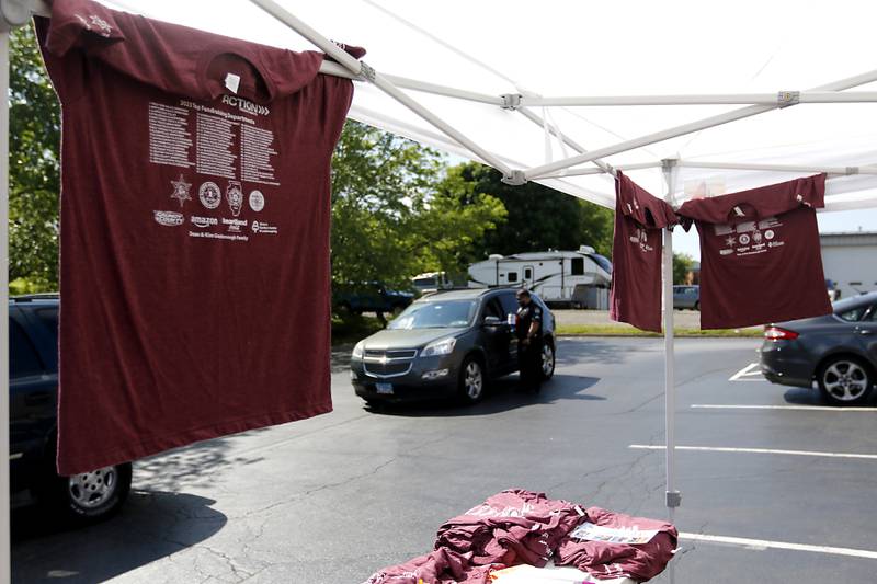 Torch Run t-shirts are displayed as a McHenry County Sheriff's officer asks for a donation during the Cop on a Rooftop fundraiser for Special Olympics Illinois on Friday, May 17, 2024, at the Dunkin’ Donuts in Woodstock. Law enforcement officers spent their morning raising funds and awareness for Special Olympics Illinois and the Law Enforcement Torch Run.