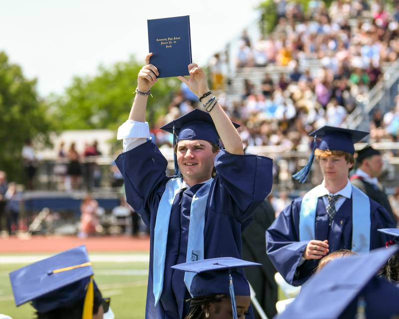 A Downers Grove South graduate holds up his diploma as he walks back to his seat during the  graduation held at Downers Grove South High School football stadium on Sunday May 19, 2024.