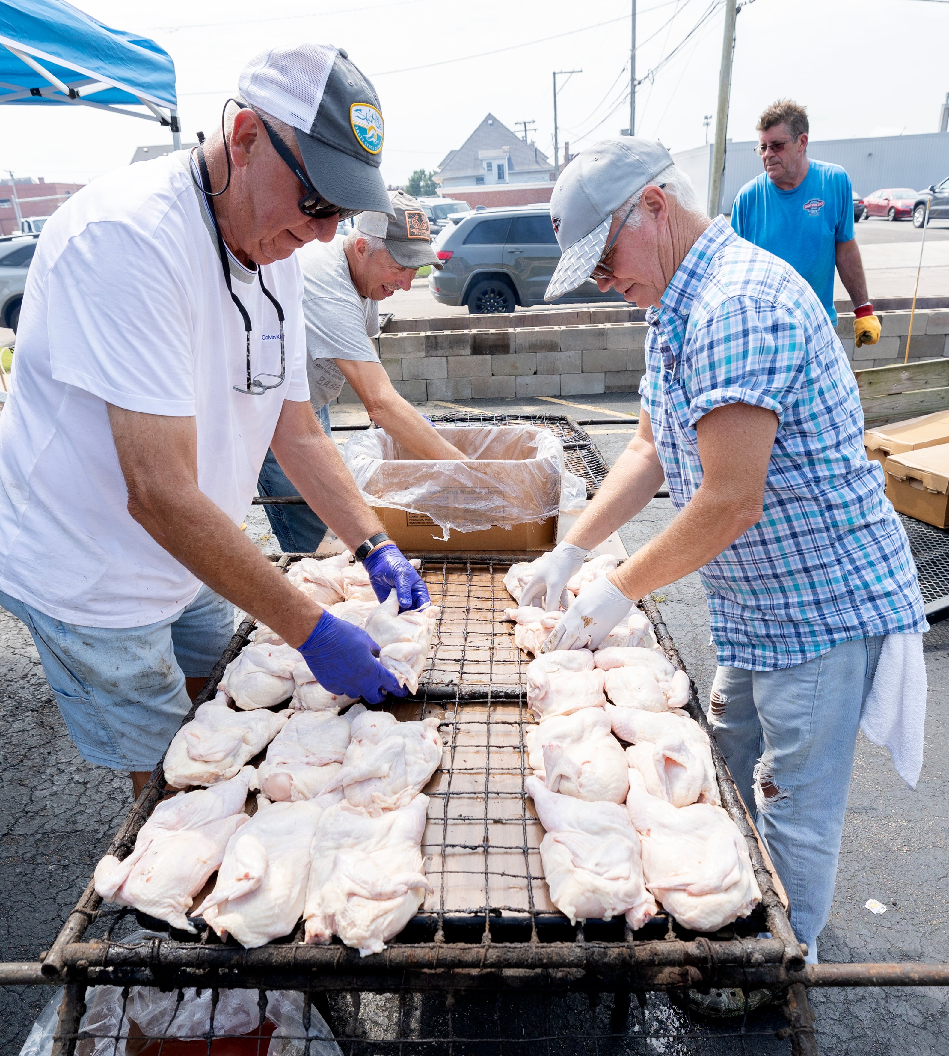 Jim Glazier (left) and Mike Wheeler lay out chicken halves on racks Monday, Aug. 5, 2024, in Sterling.