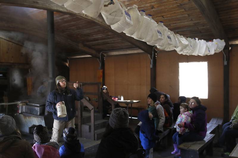 Christine Kustra points at the forty gallon jugs of sap that would be need to make one gallon maple syrup while teaching about making maple sugaring during the McHenry County Conservation District’s annual Festival of the Sugar Maples, at Coral Woods Conservation Area, 7400 Somerset Drive in Marengo, on Monday, March 11, 2024.