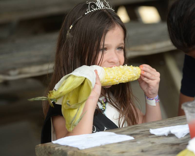 Quinn Heggen, 6, of Monroe Center, enjoys an ear of corn from the Ag in the Classroom food shed at the Ogle County Fair on Sunday, Aug. 6, 2023. Quinn was named Little Miss Ogle County earlier in the week.