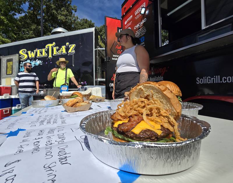 Alexis Peplow of Bat 17 from Evanston awaits customers Saturday, Sept. 14, 2024, in the shadows of one of their crafted burgers during the Fall Food Truck Festival in Streator's City Park