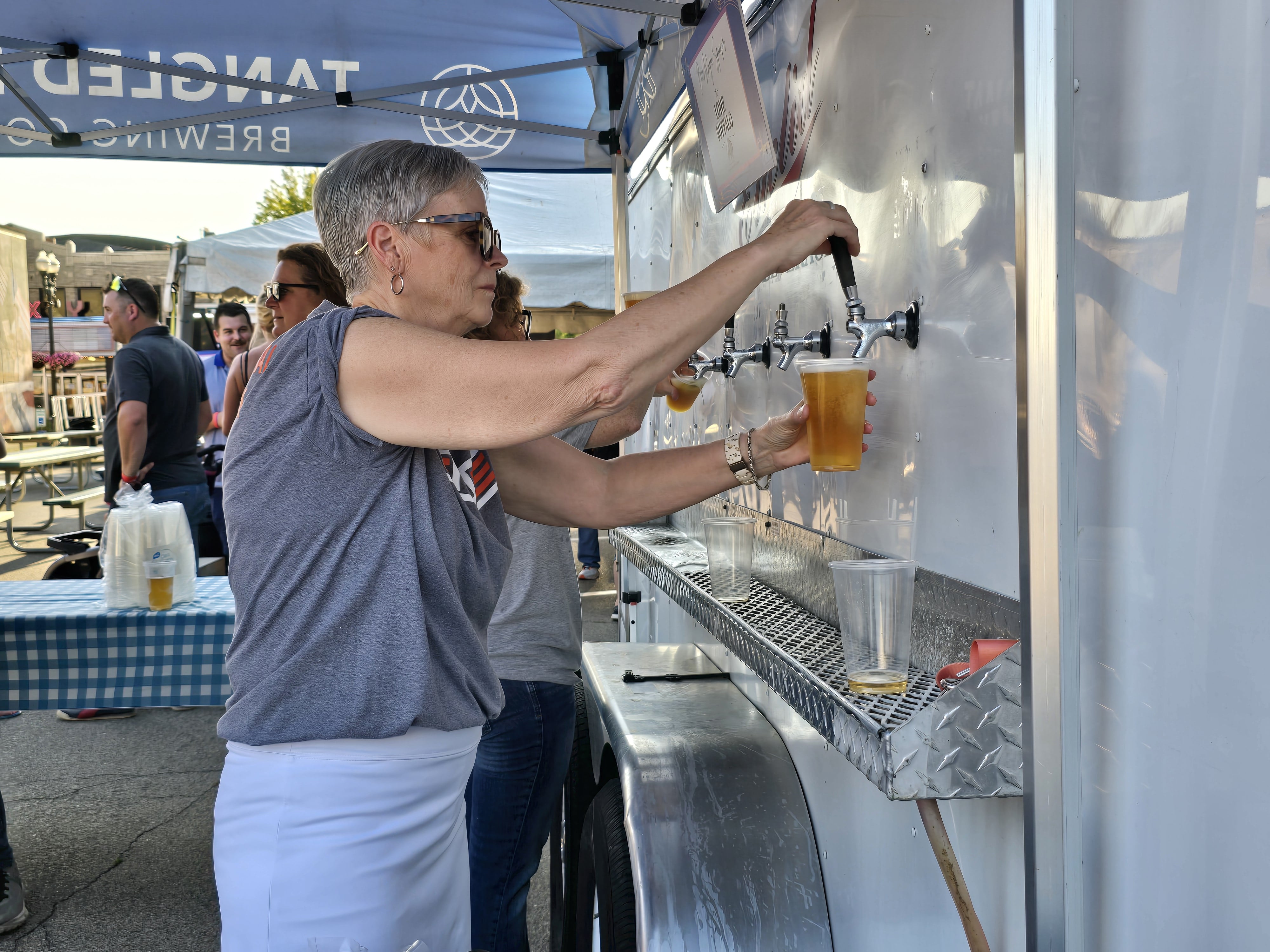 Diane Markey, of Financial Plus Credit Union, volunteers pouring beer Wednesday, July 31, 2024, at the Rock the Block Ottawa Area Chamber of Commerce event on Jackson Street.