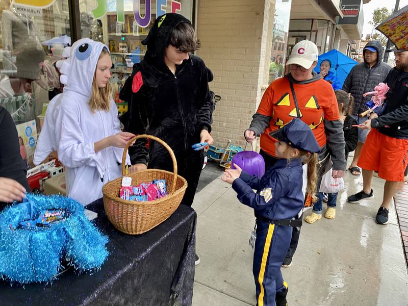 Police officer Emma Holliday, 7, of DeKalb, joined by her mother Brittani Holliday, gets a piece of candy outside Kids Stuff store, 149 E. Lincoln Highway, in downtown DeKalb Thursday, Oct. 26, 2023 during the 26th annual Spooktacular hosted by the DeKalb Chamber of Commerce.