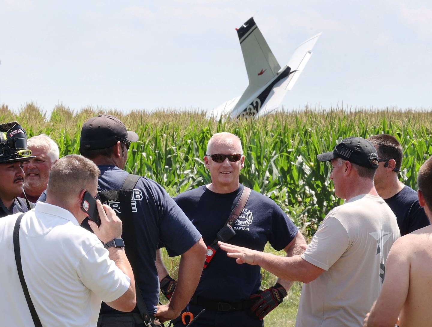 First responders talk as the tail section of a crashed plane protrudes from a cornfield Thursday, July 27, 2023, behind a business at 260 West Lincoln Highway in Cortland.