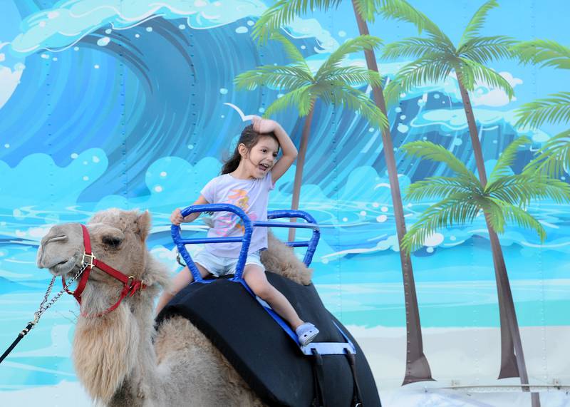 Five-year-old Jazmyn Soto of Aurora is thrilled to be riding on the back of a camel at the Hog Diggity Dog show ring during the Oswegoland Park District's PrairieFest on Friday, June 14, 2024.