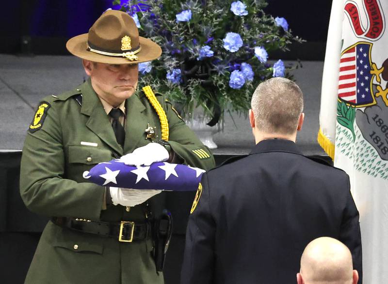 An Illinois State Police officers gives the flag from the casket of DeKalb County Sheriff’s Deputy Christina Musil to Sheriff Andy Sullivan to pass along to her family Thursday, April 4, 2024, during her visitation and funeral in the Convocation Center at Northern Illinois University. Musil, 35, was killed March 28 while on duty after a truck rear-ended her police vehicle in Waterman.