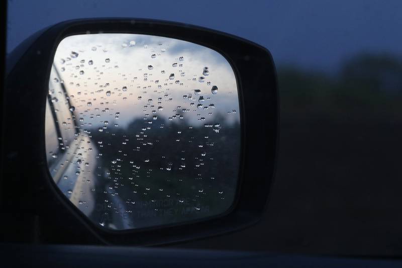 Rain drops cling to a car mirror on a rainy blue Monday.