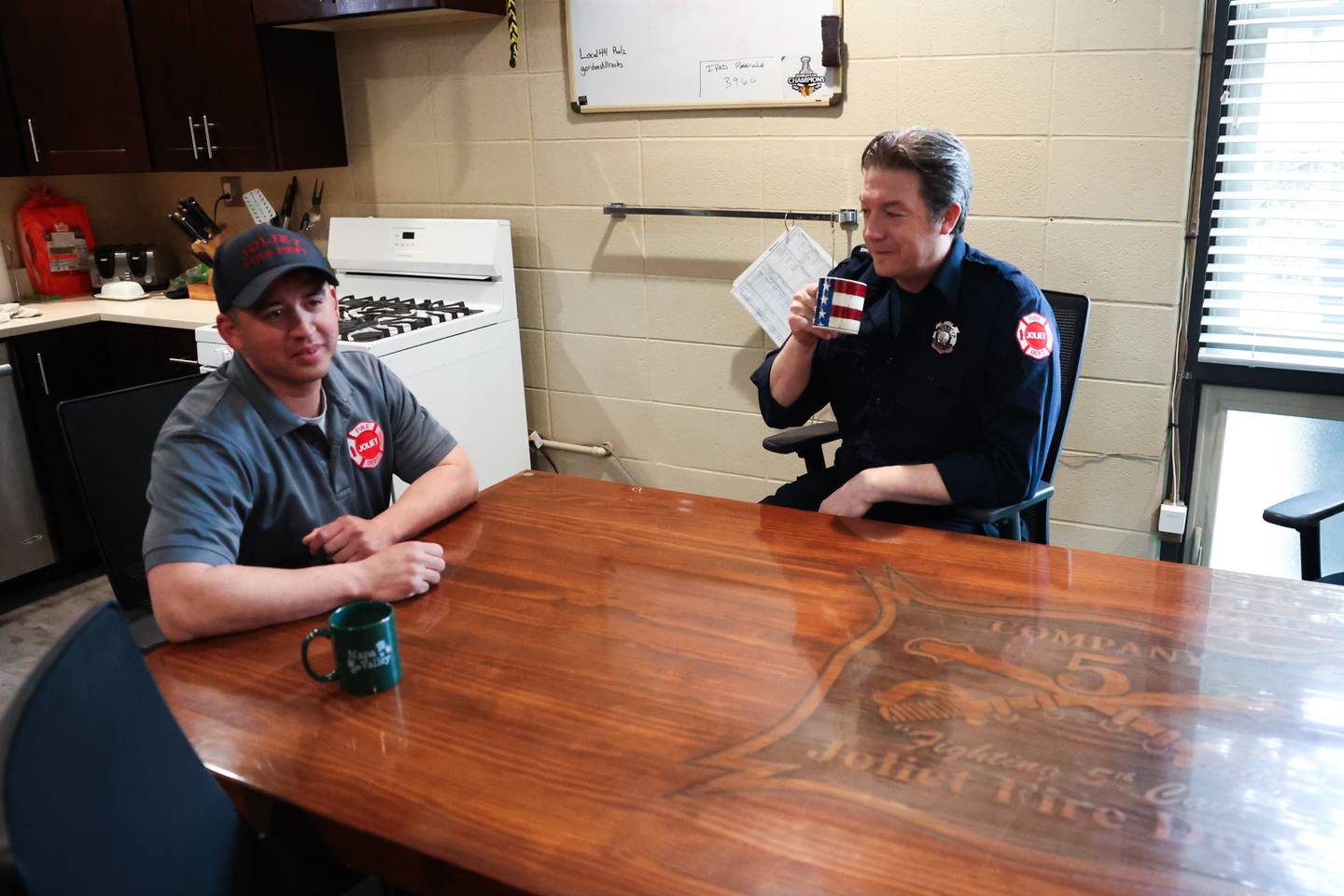 Joliet Firefighter Chris “coach” Kinsella, right, sits with fellow firefighter Aaron Aguirre on Thursday, April 11. Kinsella is the defensive line coach for Joliet Catholic’s football which earned him the nickname “coach” at the station.