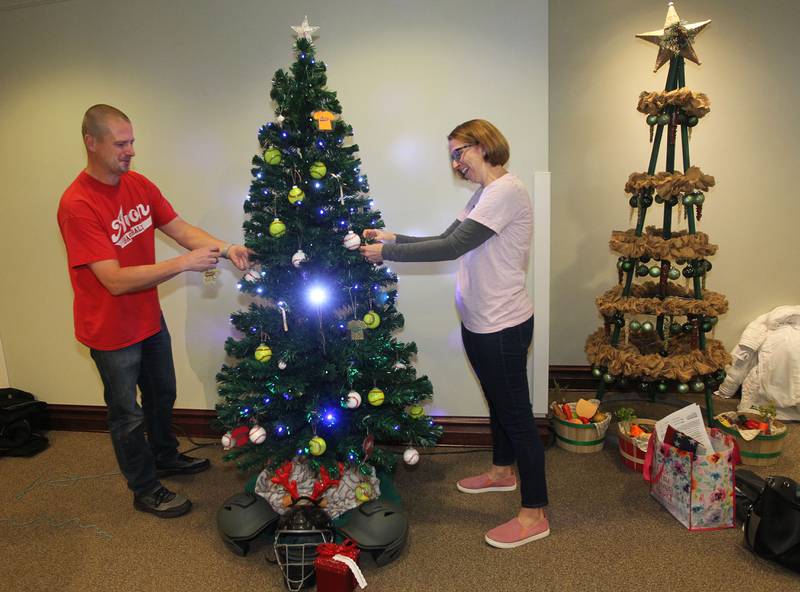 Dan Novacek, of Round Lake Beach and Elaine Ross, of Round Lake hang ornaments on the Avon Township Youth Baseball & Softball tree which will be on display in the Giving Trees exhibit at the Grayslake Heritage Center & Museum.