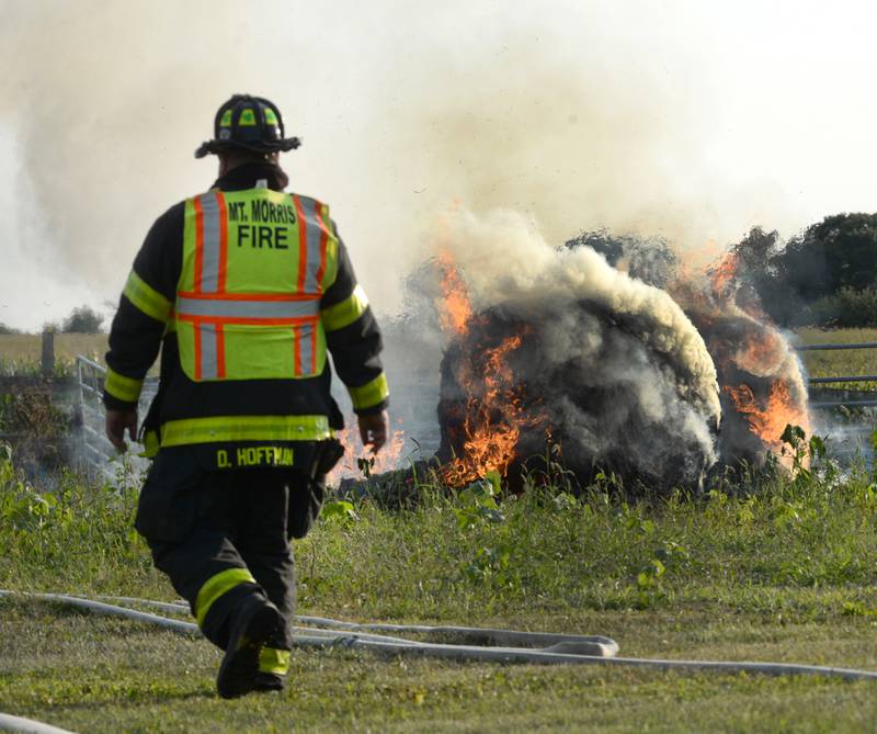 Mt.Morris firefighter David Hoffman walks by a  burning round bale of hay during a large machine shed fire at 7015 W. Judson Road, southeast of Polo, Monday evening, Sept. 10, 2024. Several fire departments assisted the Polo Fire Department on the call. There were no injuries.