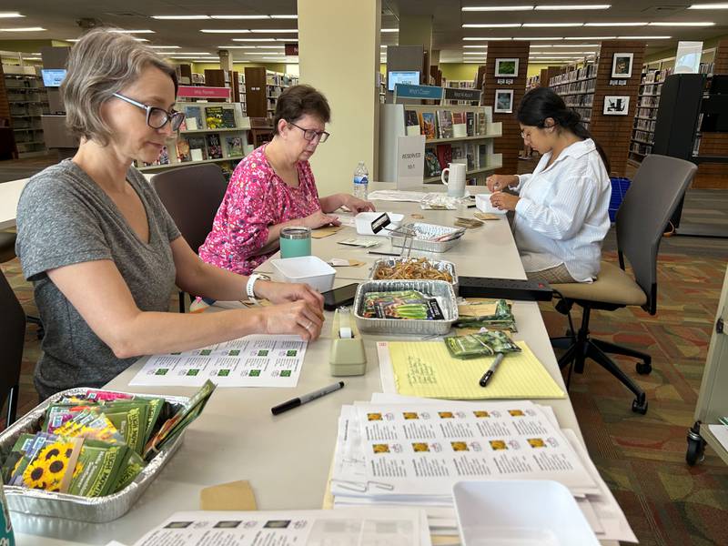 Crystal Lake Public Library's Megan Smith, left, fills seed packets with help from volunteers.