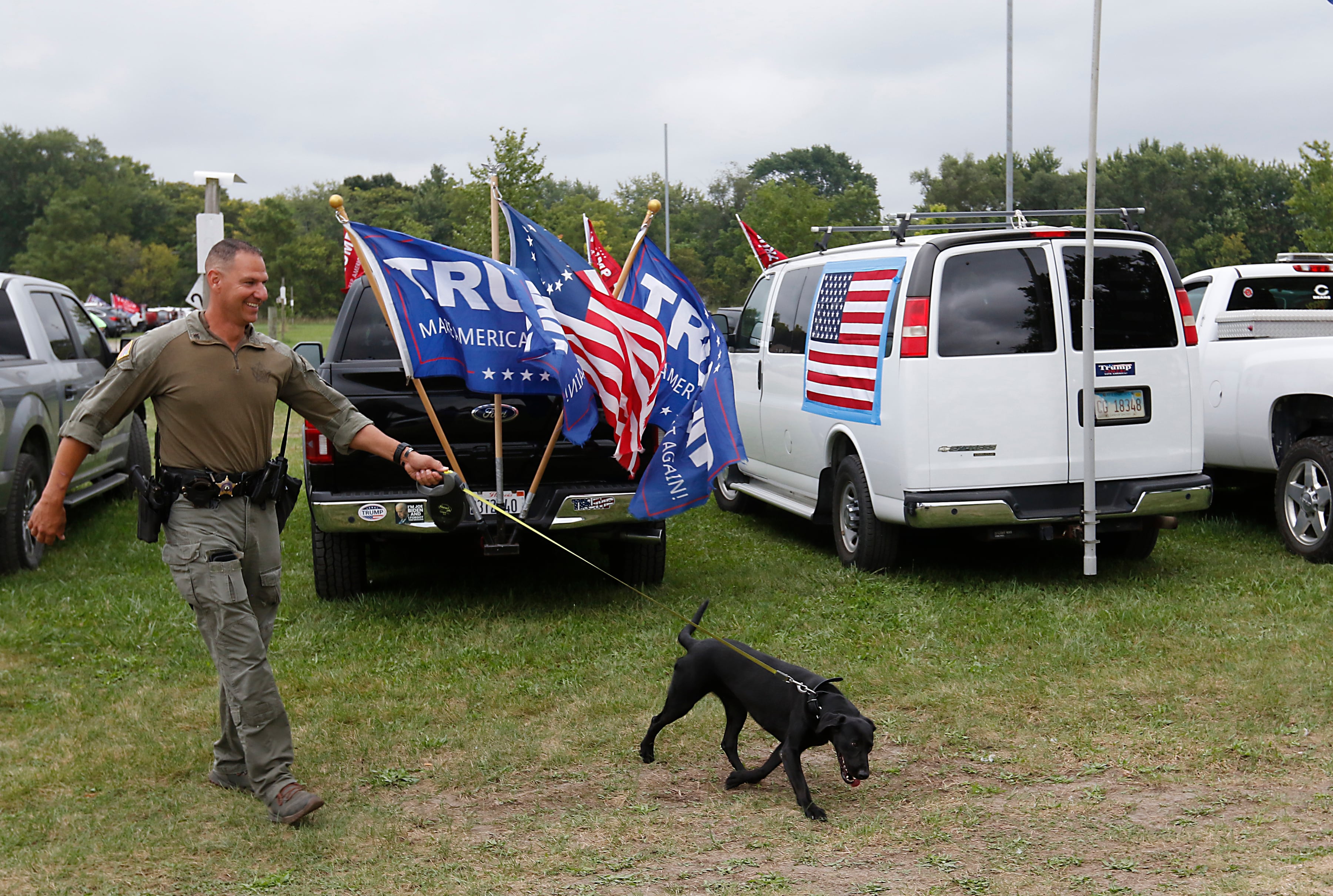 A Kane County sheriff deputy and his K9 partner check cars in the parking lot during the Trump Now-Save the American Dream Rally at the McHenry County Fairgrounds on Sunday Aug. 18, 2024, in Woodstock.