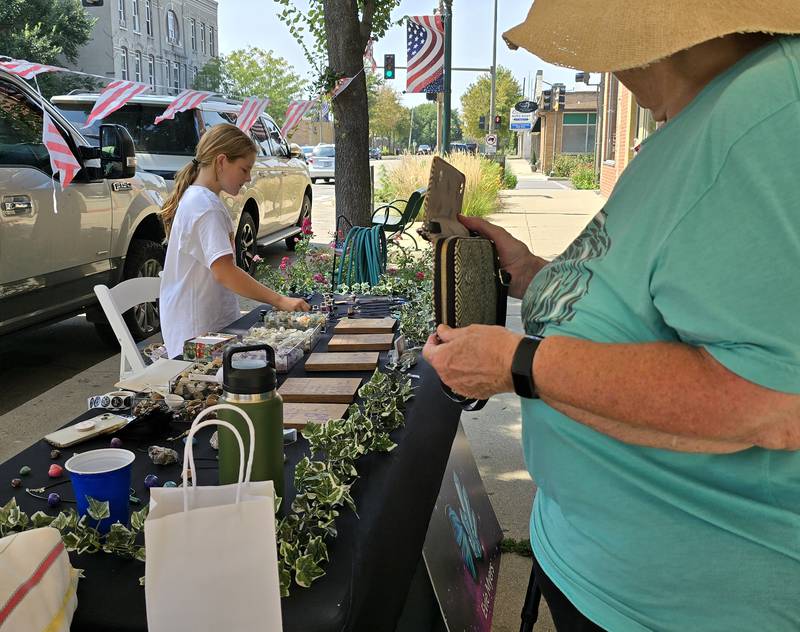 Evie Myers of Plainfield prepares a purchase from a customer Saturday, Aug. 24, 2024, at RAE Creations USA the third annual Prairie Fox Books Children's Business Fair in downtown Ottawa.