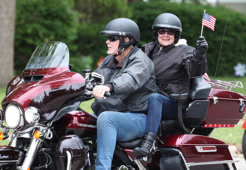 Motorcyclists leading the procession wave flags as they make the turn onto Linden Place from West Locust Street during the DeKalb Memorial Day parade Monday, May 27, 2024, on their way to Ellwood House for the ceremony.