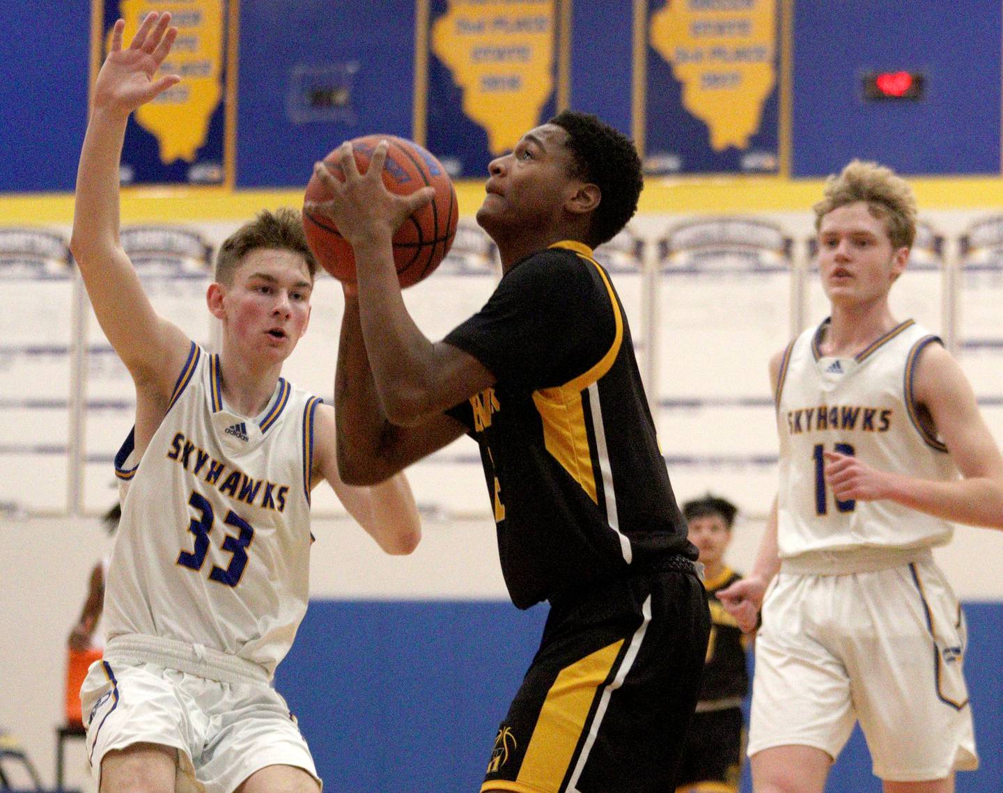 Harvard’s DeAndre Keller, center, takes a shot as Johnsburg’s JT Schmitt, left, defends in varsity boys basketball at Johnsburg Saturday.