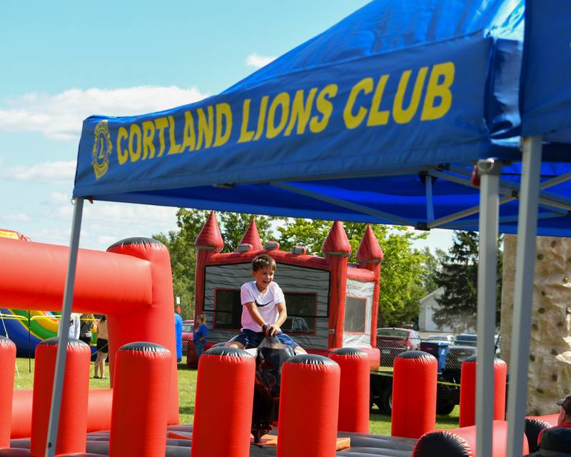 A young community member rides a mechanical bull near the Cortland Lions Club tent during Cortland Summerfest held at Cortland Community Park on Saturday, Aug. 10, 2024. .