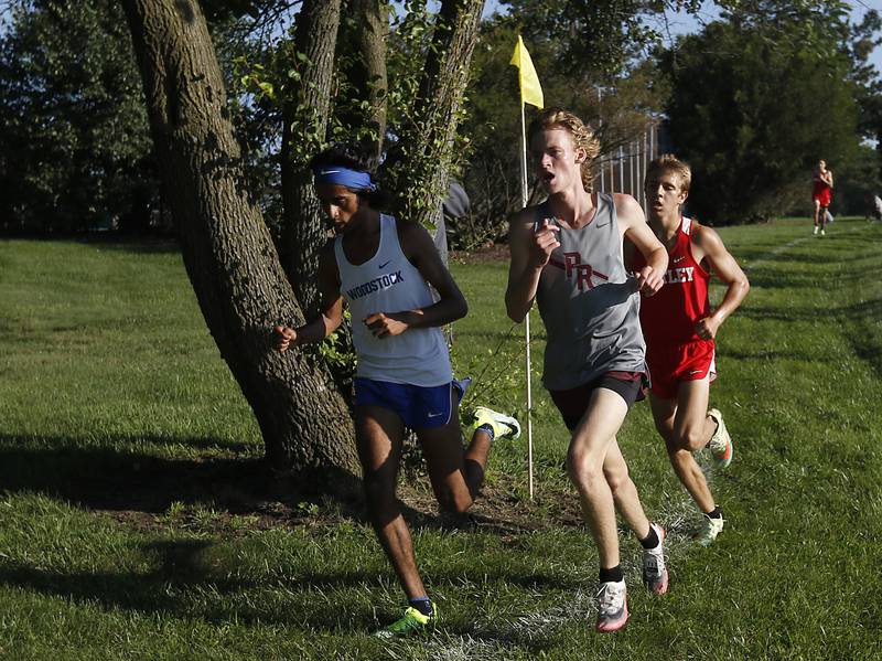 Woodstock’s Ishan Patel, Prairie Ridge’s Will Gelon and Huntley’s Tommy Nitz, round a flag during the boys race race of the McHenry County Cross Country Meet Saturday, August 27, 2022, at Emricson Park in Woodstock.