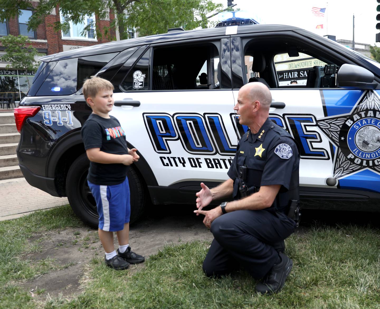 Batavia Police Chief Shawn Mazza chats with Bronson Wing, 7, while handing out coupons for free scoops of ice cream outside the Batavia Creamery on Thursday, June 6, 2024.