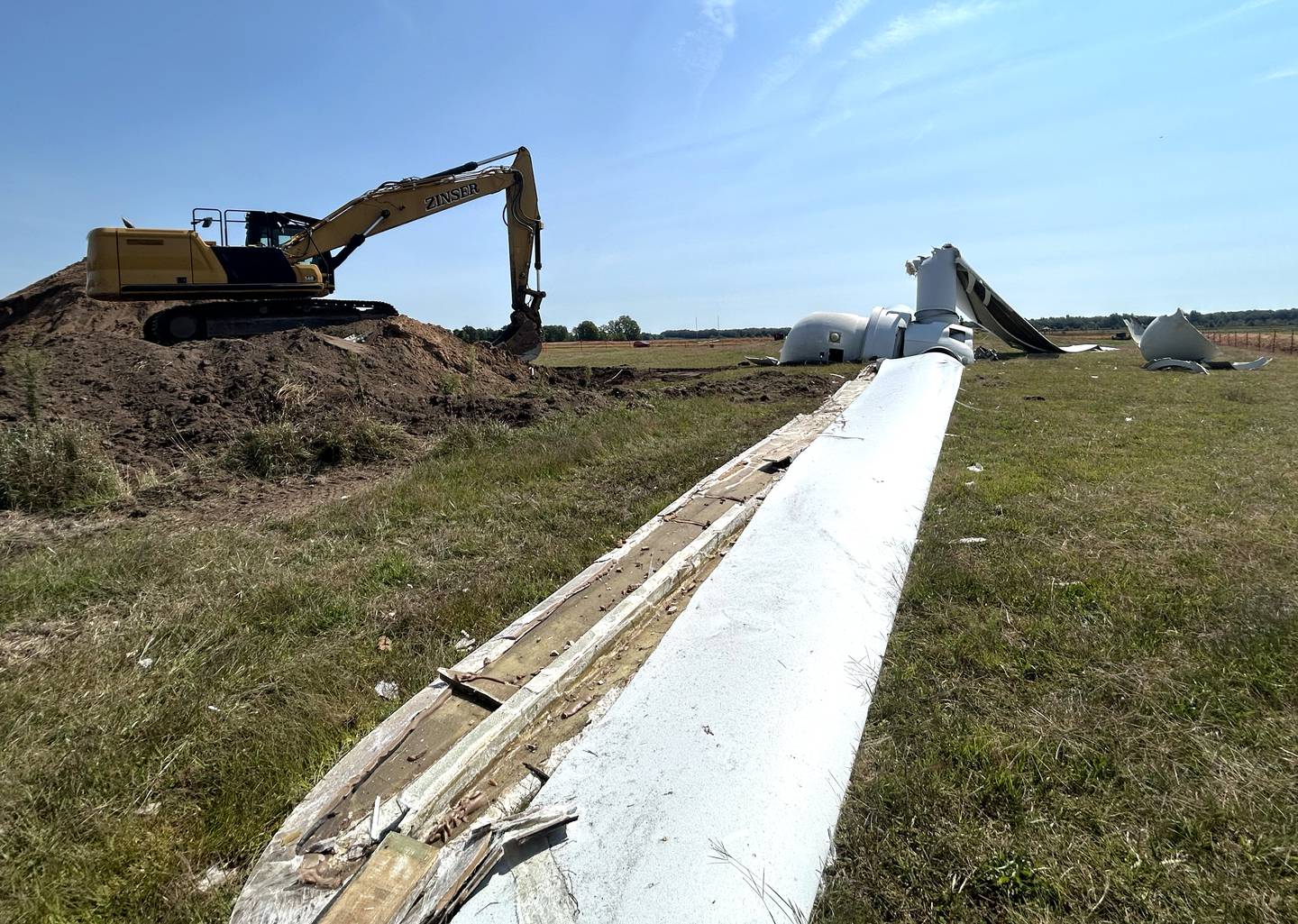 One of the 90' long blades of the wind turbine lays on the ground by Erie Middle School on Thursday, Sept. 5, 2024 after workers for DW Zinser pulled down the 200' turbine on Sept. 4 with the excavator pictured at left. The Erie School Board voted in July to demolish the nonoperational turbine.