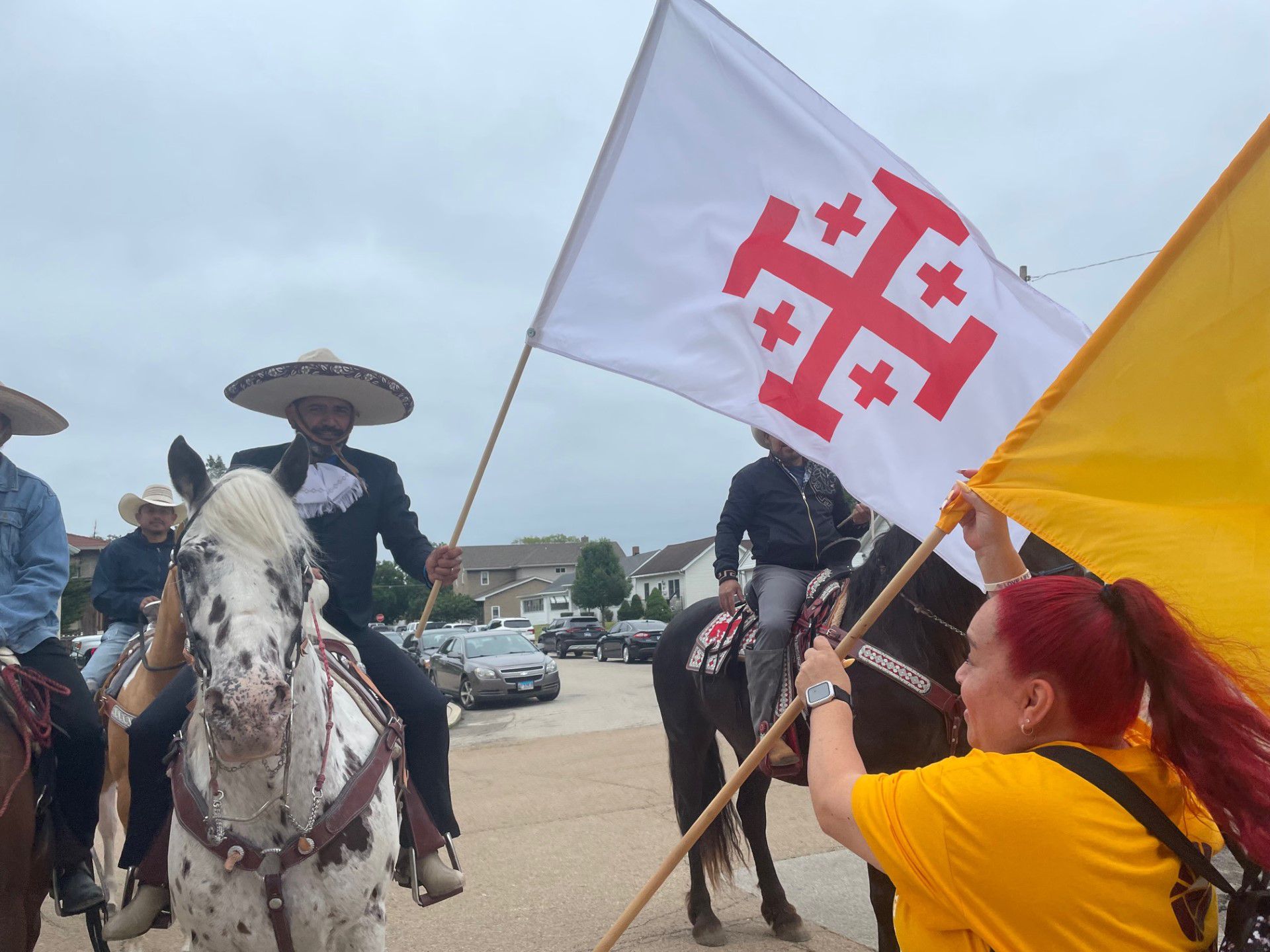 Esmeralda Cruz (right) hands flags bearing the Jerusalem Cross and the papal insignia to equestrians who agreed to ride ahead of the annual Corpus Christi procession on Sunday, June 11, 2023.