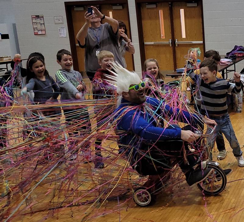 Geneva District 304 Mill Creek Elementary School’s first grade students shower their principal, George Petmezas with confetti streamers. The principal promised to ride a tricycle through the cafeteria if they raised $10,000 during a read-a-thon – and they raised $14,500.