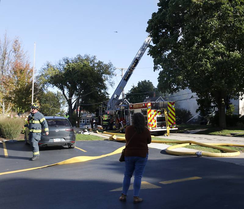 People watch as firefighters battle a house fire in the 300 block of Lincoln Avenue in Woodstock Monday, Oct. 9, 2023, after an explosion following suspected gas leak in the area.