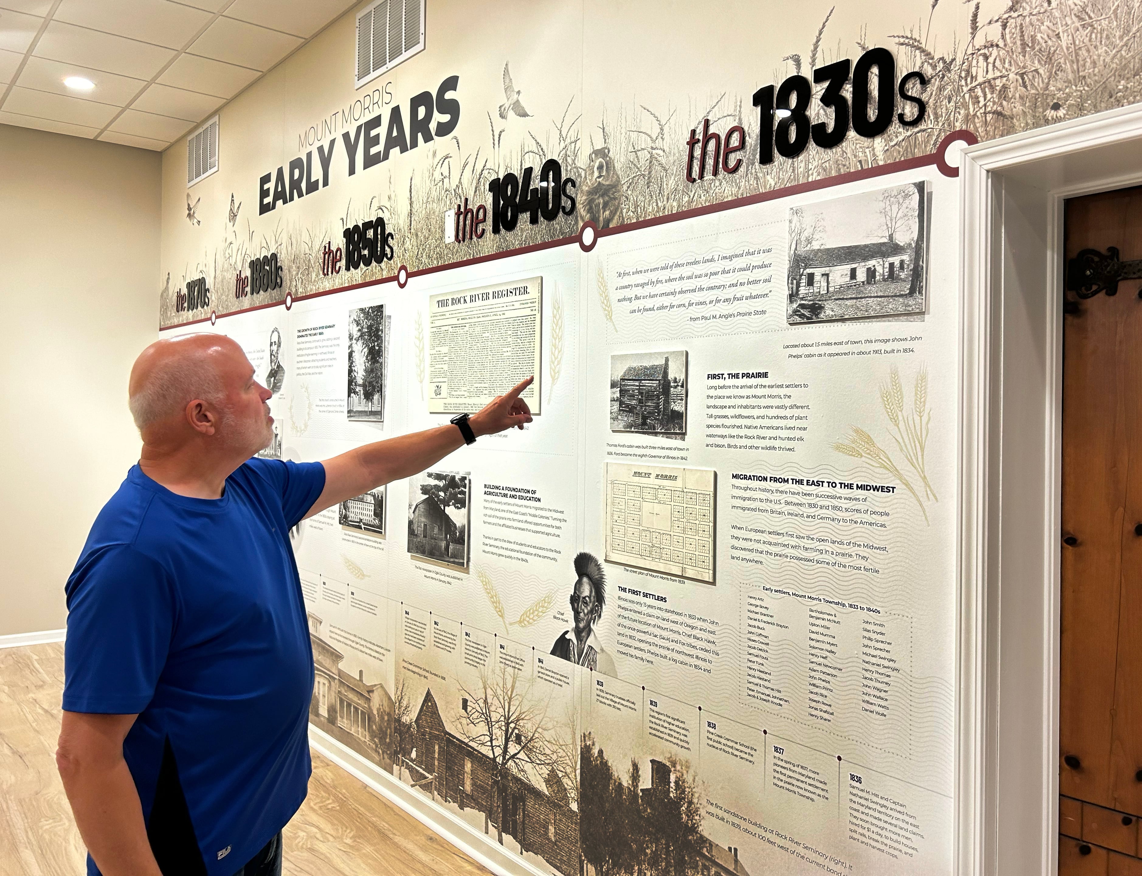 Mt. Morris Historical Committee chairman Howie Herman points on Friday, June 21, 2024, to the historical timeline on one the walls in College Hall, the former Kable News Company building on the historic campus square in downtown Mt. Morris.