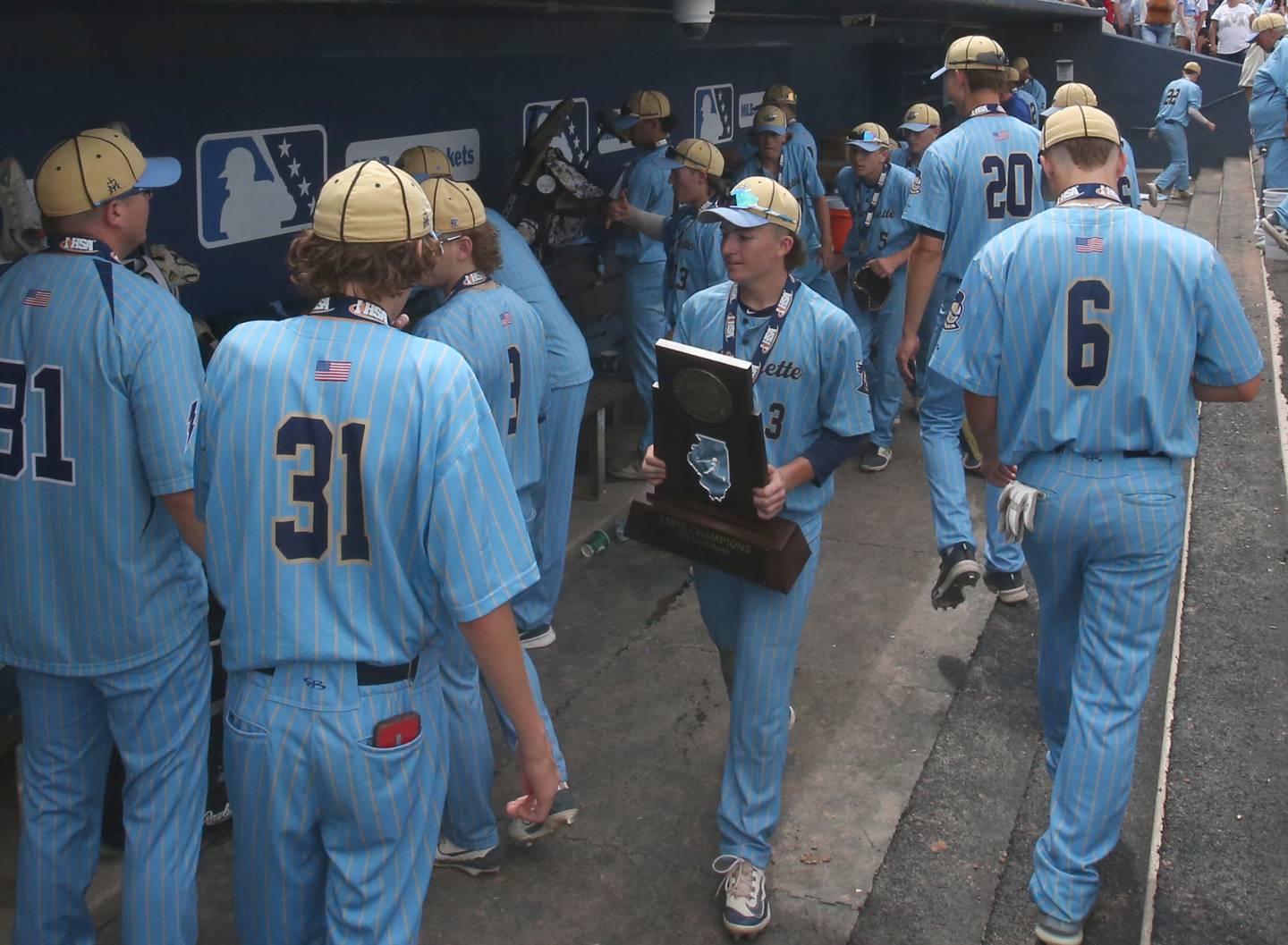 Marquette's Carson Zellers clings onto the Class 1A championship trophy while walking through the dugout after defeating Altamont 6-2 on Saturday, June 1, 2024 at Dozer Park in Peoria.