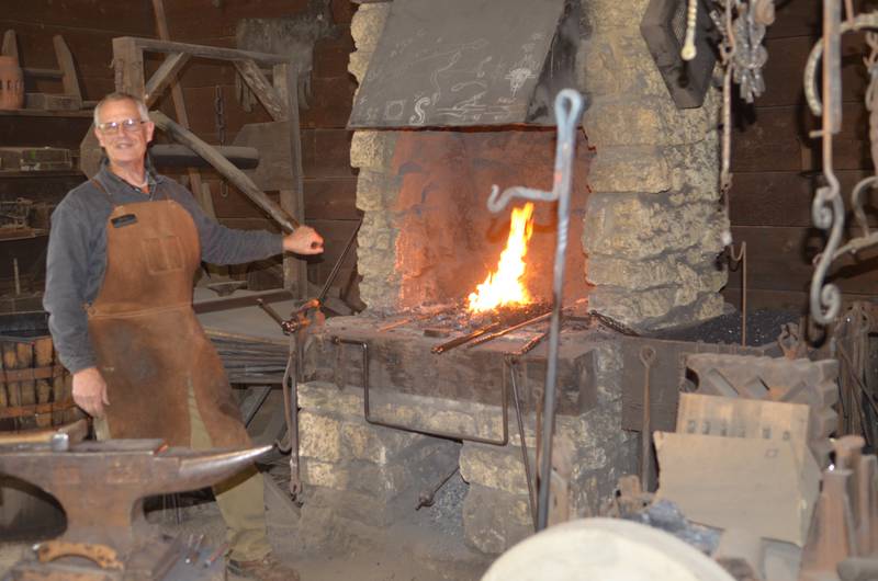 Greg Dutchoff pumps the bellows to increase the flames in the blacksmith's shop's fireplace Sunday at the John Deere Historic Site in Grand Detour,