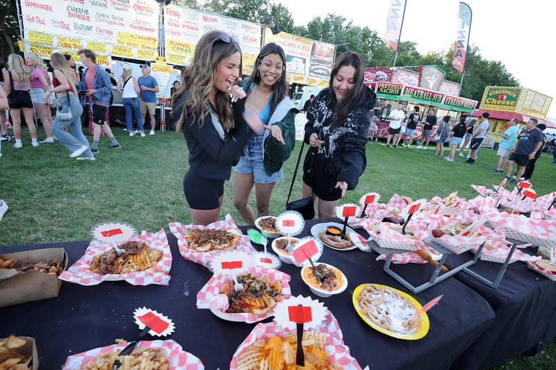 Gracie Fortson (left), Nicole Ocasio and Meredith Angelo checkout the Greco and Sons rather large menu display during the Oswegoland Park District's PrairieFest on Friday, June 14, 2024.