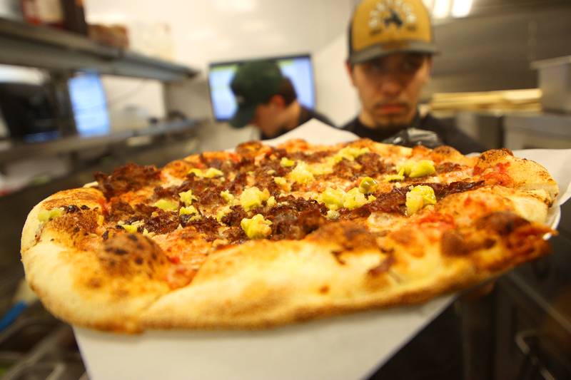 Cook Alex Farias prepares a Chicago-style cheesy beef pizza at Pickle Haus Friday night. Darryl Postelnick, known in social media circles of “Cooking With Darryl” fame, collaborated with Pickle Haus to create the special menu item.